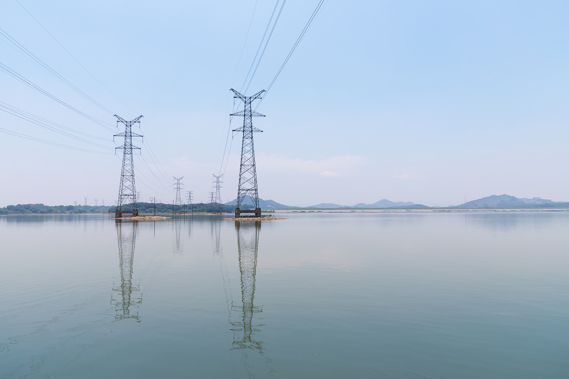 high voltage power transmission tower on lake and reflection