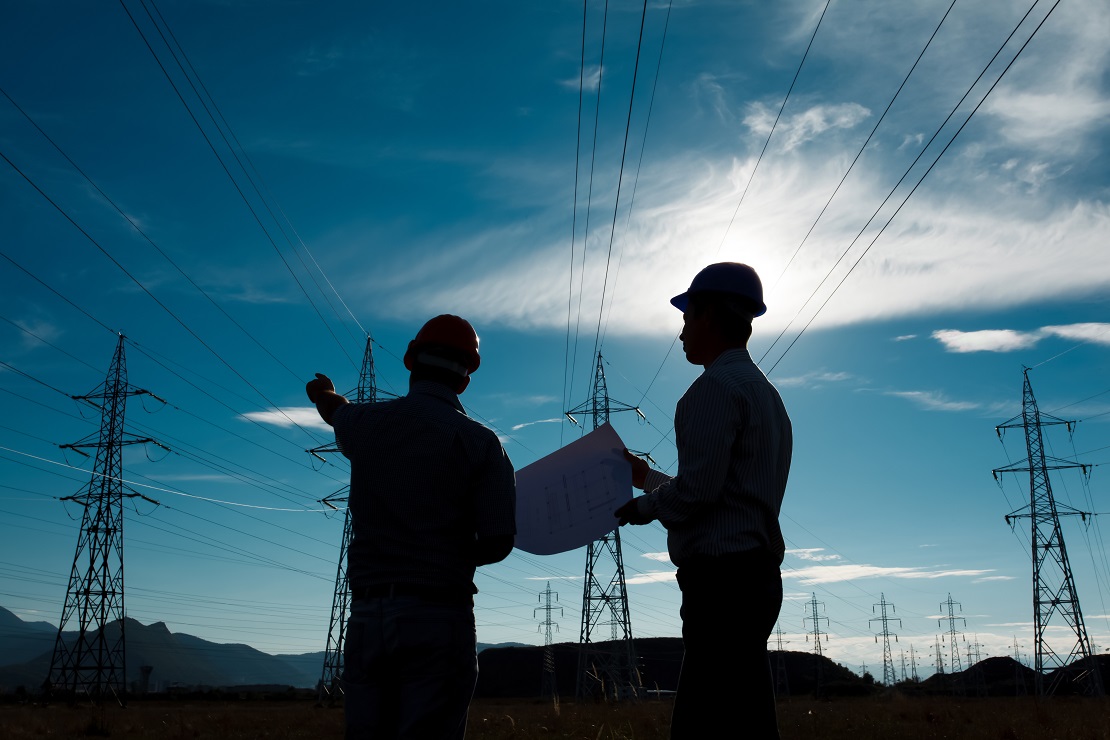 silhouette of two engineers standing at electricity station, discussing plan